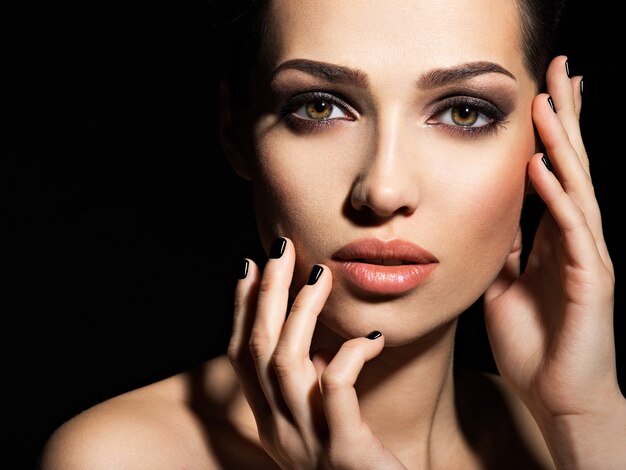 Face of a beautiful girl with fashion makeup and black nails posing at studio over dark background