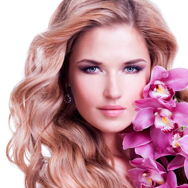 Face of beautiful woman with healthy skin and pink flower over white wall.