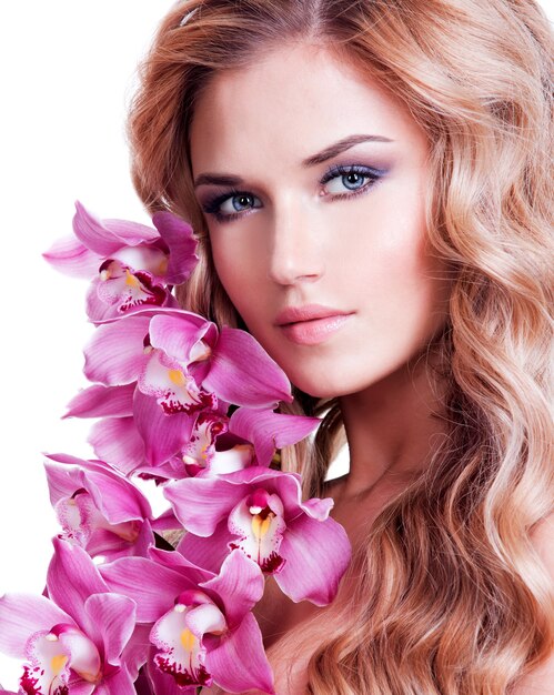 Face of beautiful woman with healthy skin and pink flower over white wall.