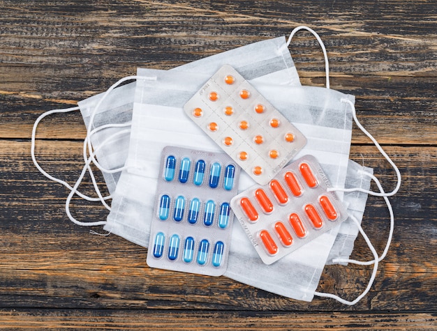 Face masks with medicine blister packs on wooden background, flat lay.