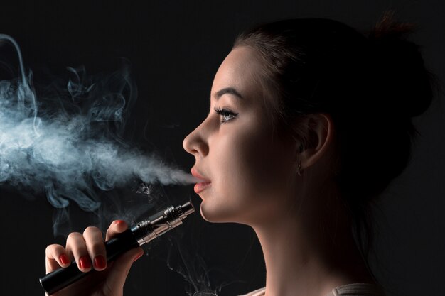 黒のスタジオでvaping若い女性の顔