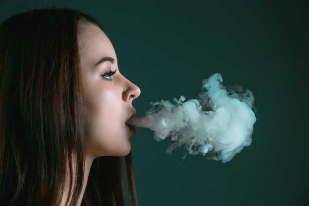 The face of vaping young woman at black studio