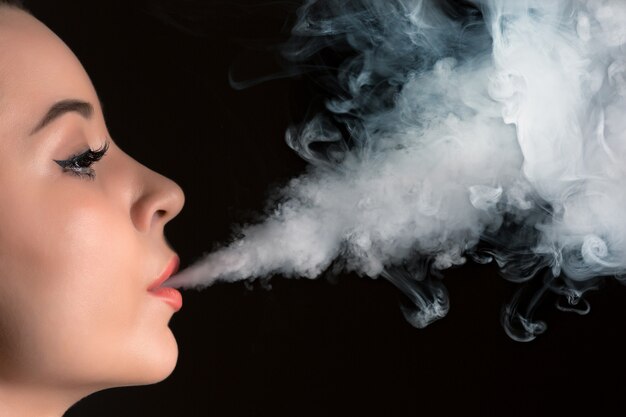 검은 스튜디오에서 vaping 젊은 여자의 얼굴