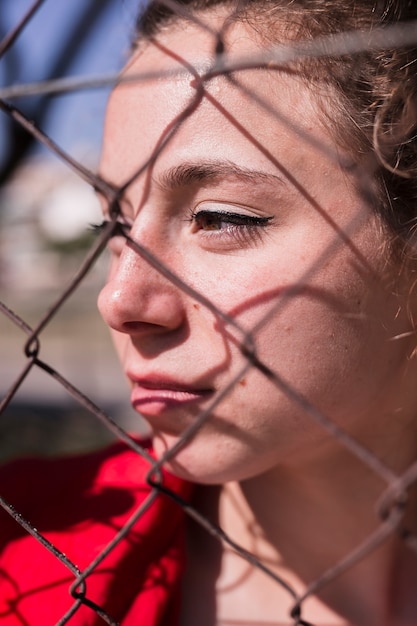 Face of young pensive girl behind metal grid