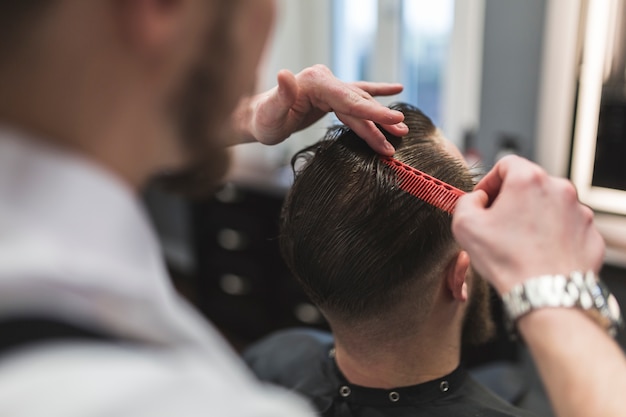 Faceless barber combing hair of man before cutting