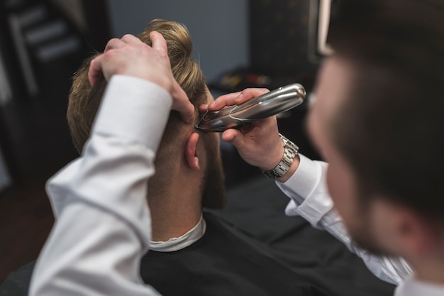 Faceless barber shaving hair of client with trimmer