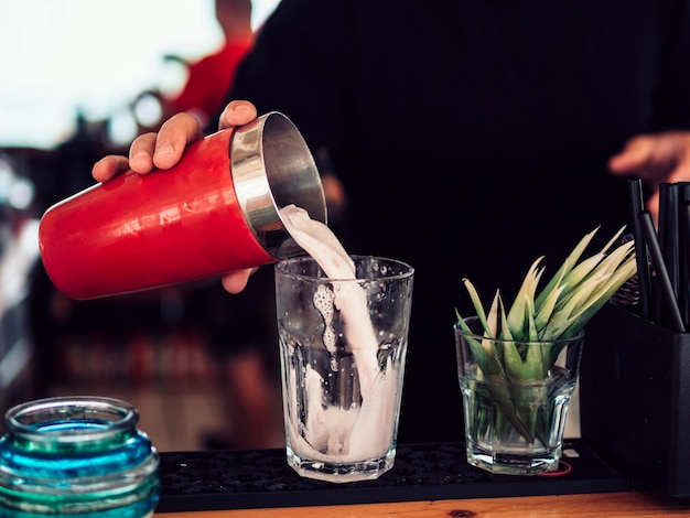Faceless bartender filling glass with milkshake in bar