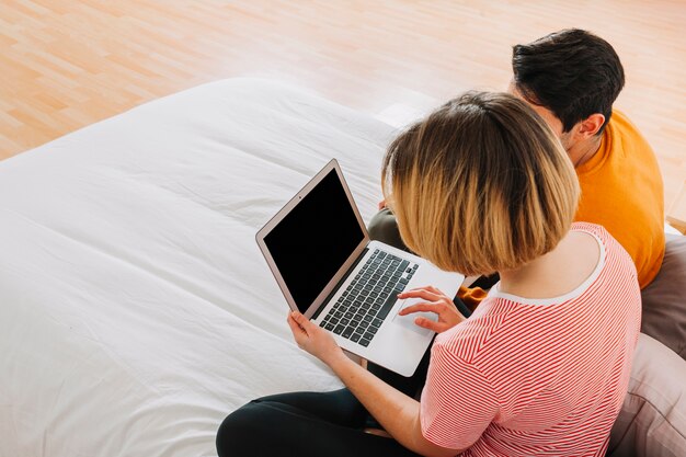 Faceless couple using laptop on bed