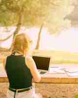 Free photo faceless female sitting and working on laptop in picturesque place