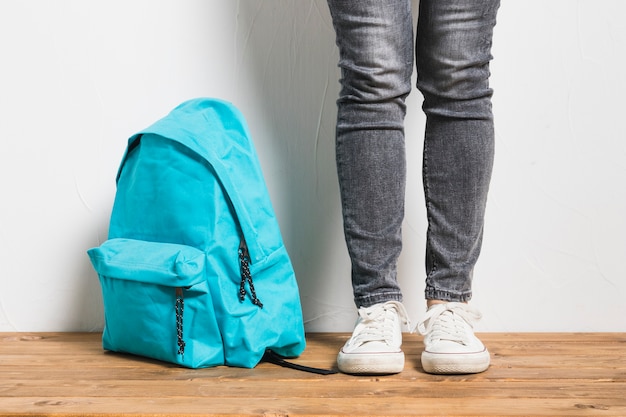 Faceless person standing beside of schoolbag on wooden table  