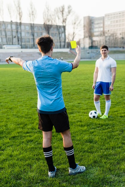 faceless referee showing yellow card to sportsman