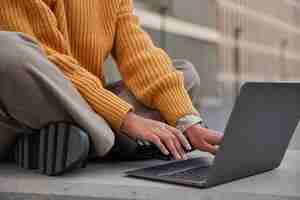 Бесплатное фото Безликая женщина сидит со скрещенными ногами на современном ноутбуке, носит теплый вязаный свитер, устанавливает приложение из сети, просматривает веб-сайт, подключенный к wi-fi freelace и концепция удаленной работы