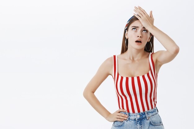 Facepalm gesture. Portrait of unhappy displeased and annoyed young arrogant woman in striped top facepalming with irritation breathing out with opened mouth and rolling eyes