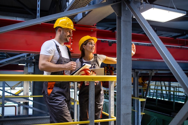 Factory engineers in protective equipment standing in production hall and sharing ideas