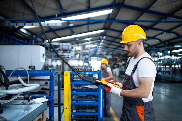 Factory worker wearing uniform and hardhat operating industrial machine with push button joystick in production hall