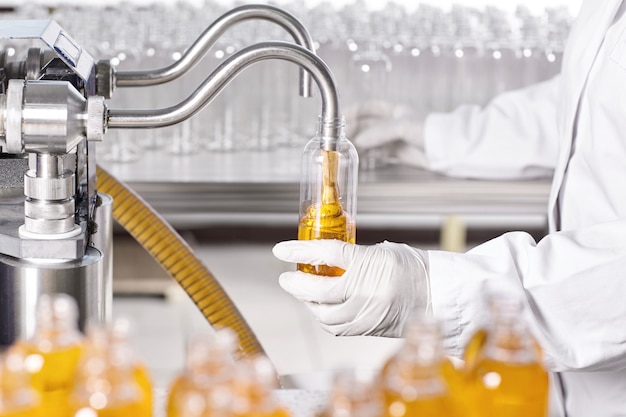 Factory worker in white gown and rubber gloves holding plastic bottle