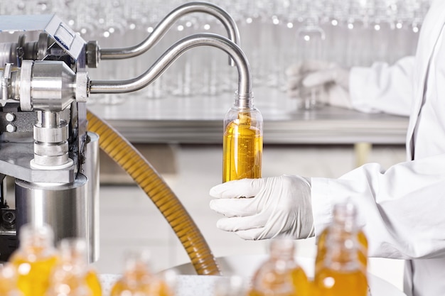 Factory worker in white gown and rubber gloves holding plastic bottle