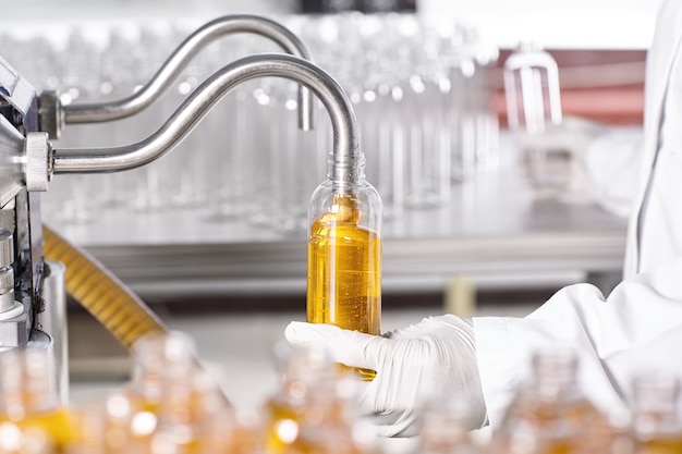 Factory worker in white gown and rubber gloves holding plastic bottle