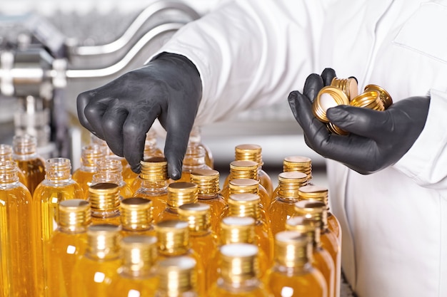 Factory worker in white gown and rubber gloves screwing bottle caps