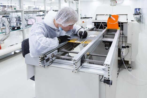 A factory worker in a white lab suit and latex gloves working with a soldering iron and some modern equioment