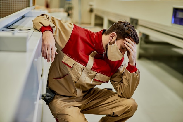 Foto gratuita operaio con maschera facciale che si sente male e tiene la testa dolorante nell'impianto di produzione