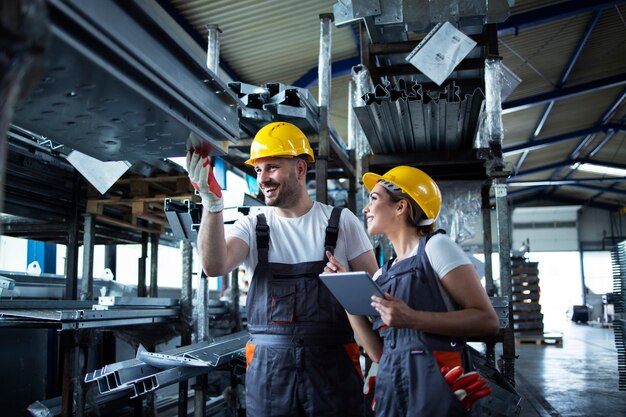 Factory workers checking inventory with tablet computer in industrial warehouse full of metal parts