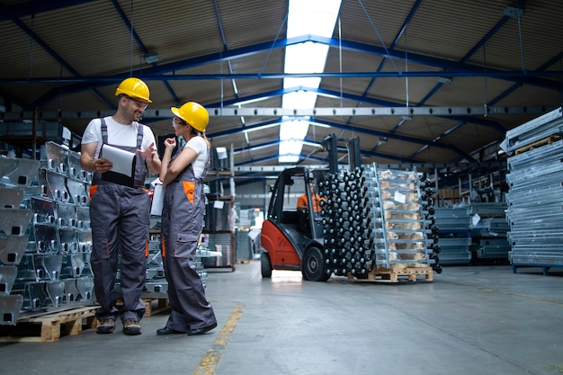 Free photo factory workers standing in industrial warehouse and discussing about production