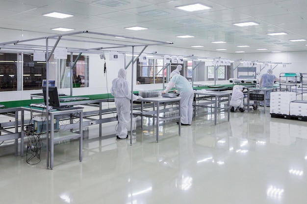 Factory workers in white lab suits producing tv sets on assebly line with some modern equipment in a clean room