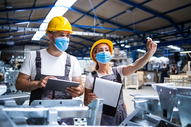 Factory workers with face masks protected against corona virus doing quality control of production in factory