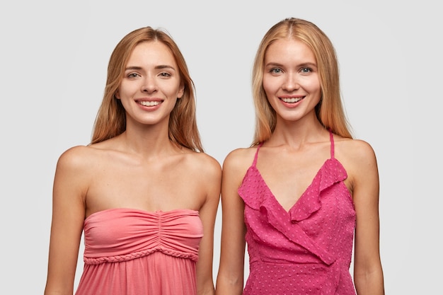 Fahionable light haired women pose for fashion magazine, dressed in pink dresses