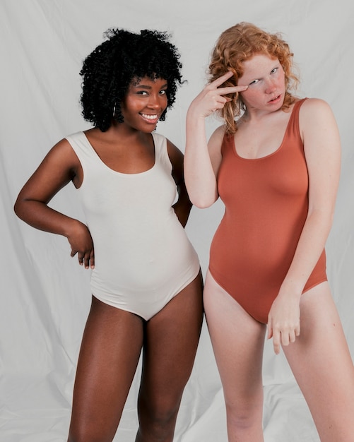 Fair and dark skinned young women standing against grey background