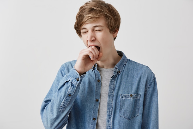 Free Photo fair-haired guy in denim shirt looking tired and sleepy, yawning, covering mouth with, after sleepless night. male student looking bored and disinterested during classes at university. body language