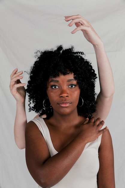 Foto gratuita mani giuste dietro la giovane donna africana che esamina macchina fotografica contro il contesto grigio