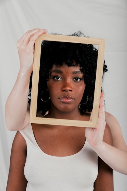 Fair skinned hands of woman holding wooden border frame in front of an african woman