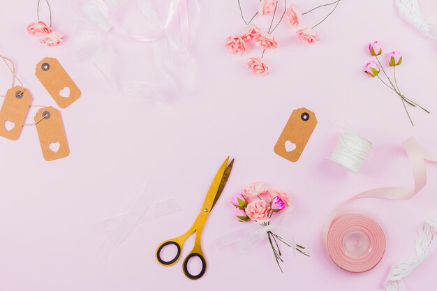 Fake artificial flowers with ribbon; tag and scissor on pink background