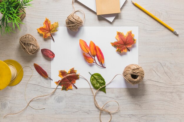 Fake autumn leaves with string spool on wooden textured background