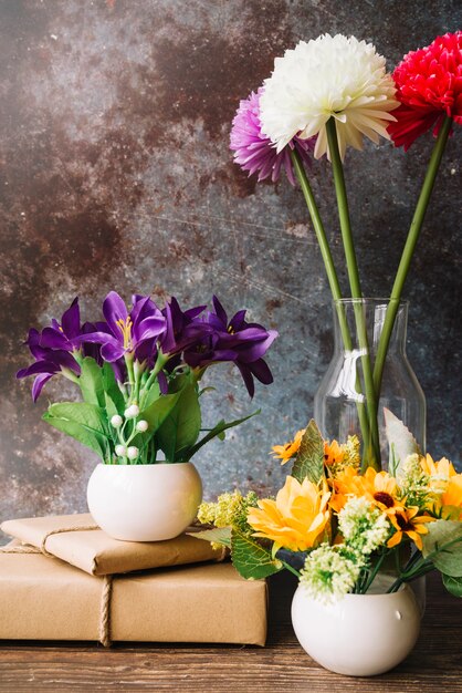 Fake flowers in different type of vase with wrapped gift boxes against grunge background