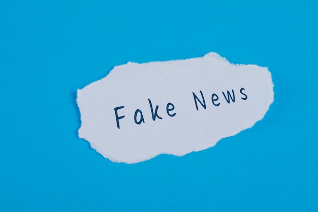 Free photo fake news text on torn paper on blue table flat lay.