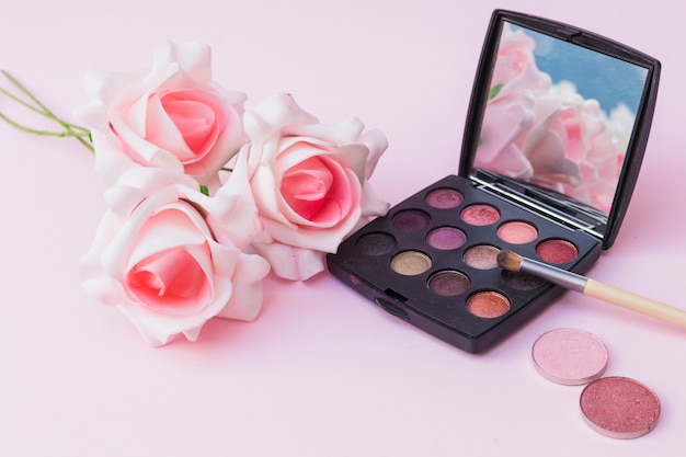 Fake pink flowers with blusher and eyeshadow palette with makeup brush