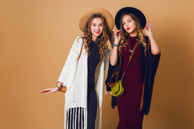 Fall  studio shot of two models  with blond wavy hairstyle in wool and straw hat wearing striped poncho