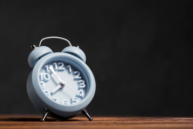 Falling blue alarm clock on wooden desk against black background