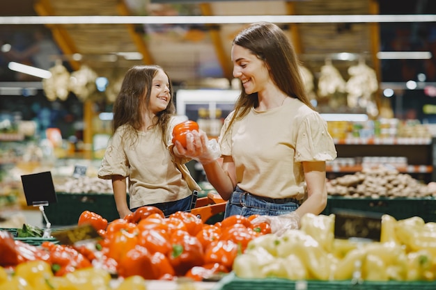 Бесплатное фото Семья в супермаркете. женщина в коричневой футболке. люди выбирают овощи. мать с дочерью.