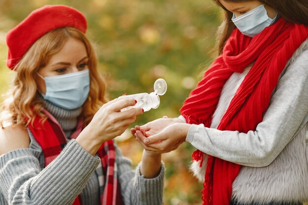 Family in a autumn park. Coronavirus theme. Mother with daughter. People use antiseptick.