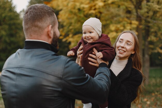 Семья в осеннем парке. Мужчина в черной куртке. Милая маленькая девочка с родителями.