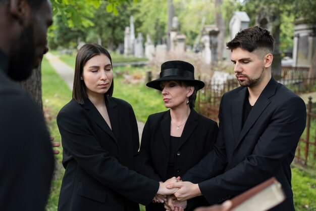 Family at the cemetery holding hands while the priest reads from the bible