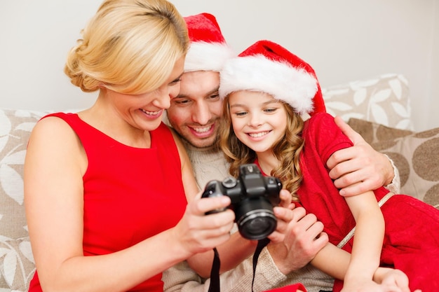 Семья, рождество, рождество, зима, счастье и люди концепция - улыбающаяся семья в шляпах санта-помощника, глядя на фотографии