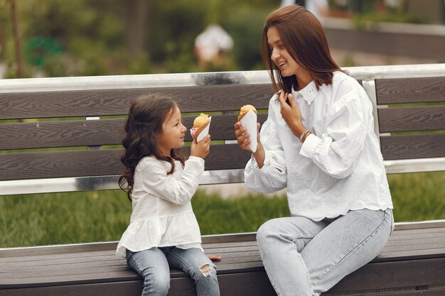 도시의 가족. 어린 소녀는 아이스크림을 먹는다. 벤치에 앉아 딸과 어머니입니다.