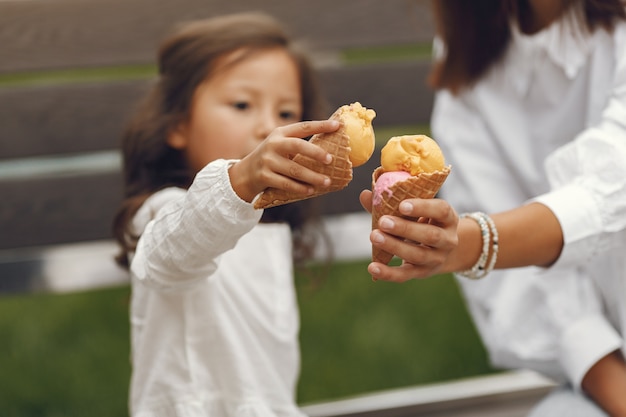 Family in a city. Little girl eats ice cream. Mother with daughter sitting on a bench.