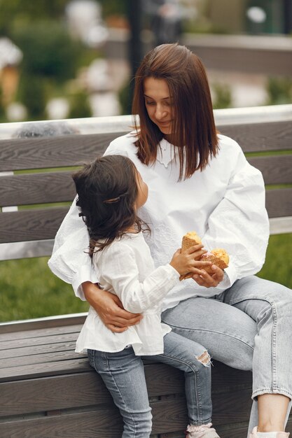 Family in a city. Little girl eats ice cream. Mother with daughter sitting on a bench.