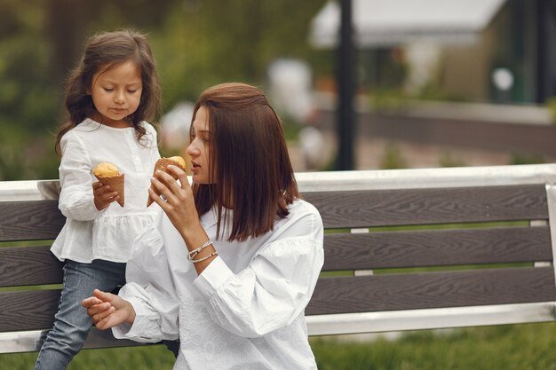 Семья в городе. Маленькая девочка ест мороженое. Мать с дочерью, сидя на скамейке.